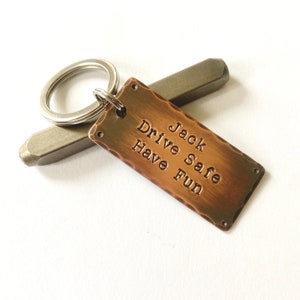 May include: A copper keychain with a hammered finish and a silver key ring. The keychain has the text "Jack Drive Safe Have Fun" engraved on it.