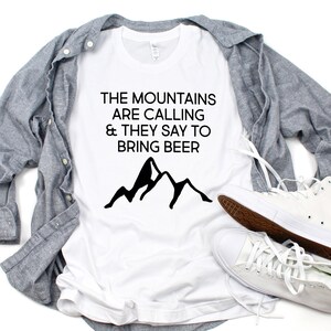 May include: White t-shirt with black text that reads "The mountains are calling & they say to bring beer". A black mountain silhouette is below the text.