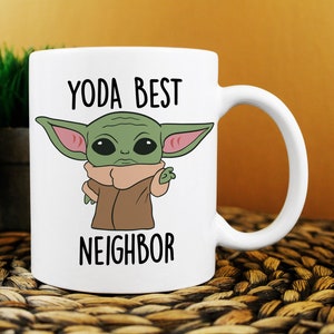 Puede incluir: Taza de cer&aacute;mica blanca con un personaje de dibujos animados verde con orejas grandes y el texto "YODA BEST NEIGHBOR" impreso en ella.