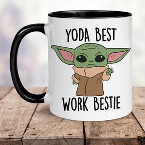 May include: White ceramic mug with a black rim and handle. The mug features a cartoon image of a green alien character with large ears and the text "YODA BEST WORK BESTIE".