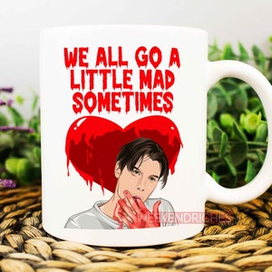 May include: White ceramic mug with a red heart and a man's face. The text on the mug reads "We all go a little mad sometimes".