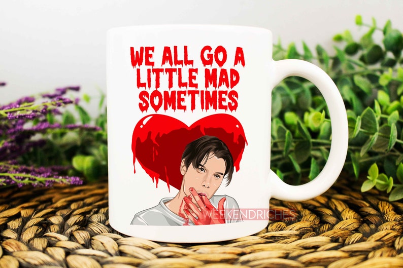 May include: White ceramic mug with a red heart and a man's face. The text on the mug reads "We all go a little mad sometimes".