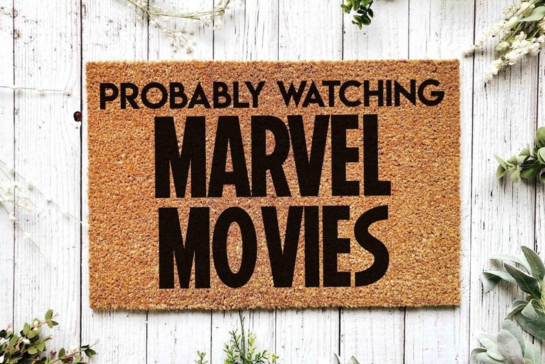 K&ouml;nnte beinhalten: Eine braune Kokosfaser-Fu&szlig;matte mit dem Text "PROBABLY WATCHING MARVEL MOVIES" in schwarzen Buchstaben.