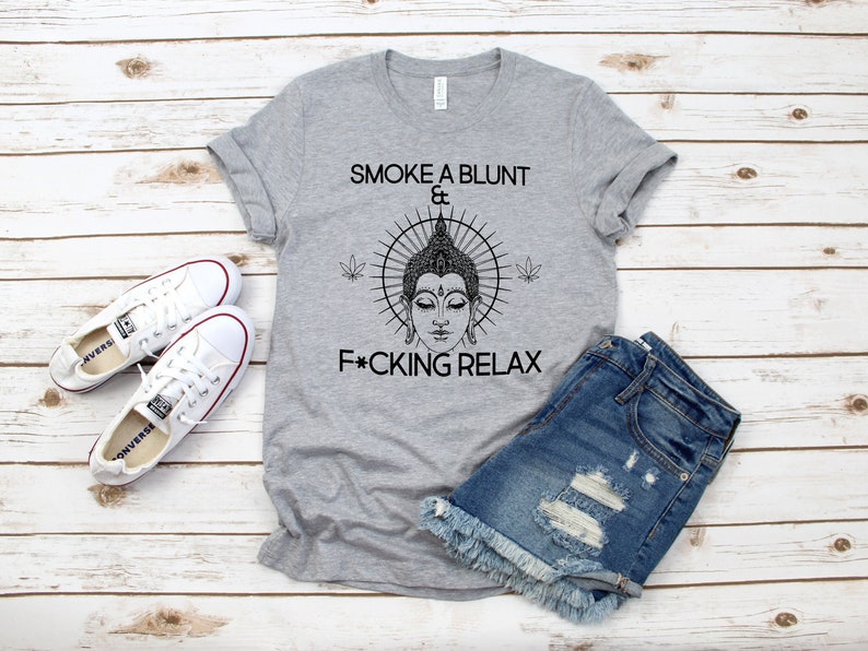 May include: A gray t-shirt with a black graphic of a Buddha head with a sunburst behind it and the text "Smoke a blunt & F*cking Relax".