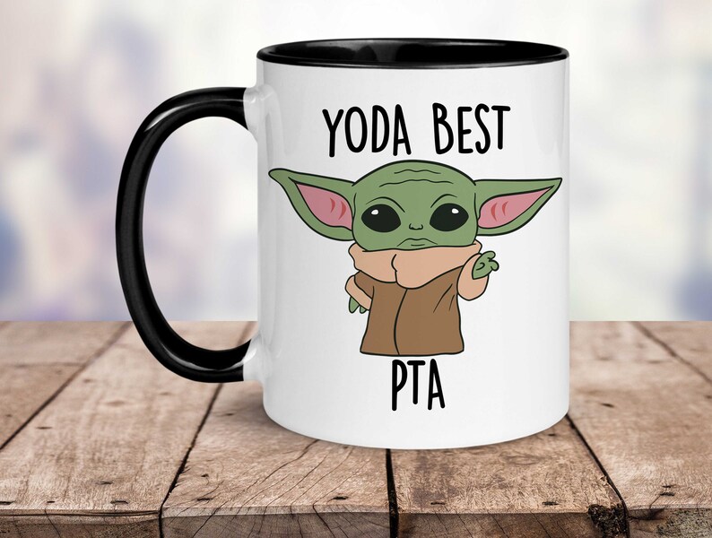 May include: White ceramic mug with a black rim and handle. The mug features a cartoon image of a green baby Yoda character with the text "Yoda Best PTA" printed on the mug.