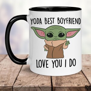 K&ouml;nnte beinhalten: Wei&szlig;e Keramiktasse mit schwarzem Rand und Henkel. Die Tasse zeigt ein Cartoon-Bild eines gr&uuml;nen Au&szlig;erirdischen mit gro&szlig;en Ohren und dem Text "YODA BEST BOYFRIEND LOVE YOU I DO".