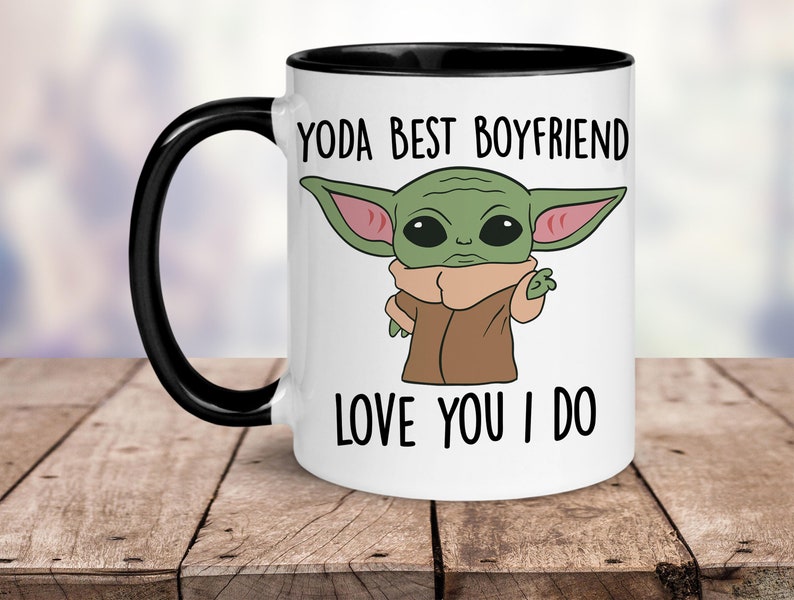 K&ouml;nnte beinhalten: Wei&szlig;e Keramiktasse mit schwarzem Rand und Henkel. Die Tasse zeigt ein Cartoon-Bild eines gr&uuml;nen Au&szlig;erirdischen mit gro&szlig;en Ohren und dem Text "YODA BEST BOYFRIEND LOVE YOU I DO".