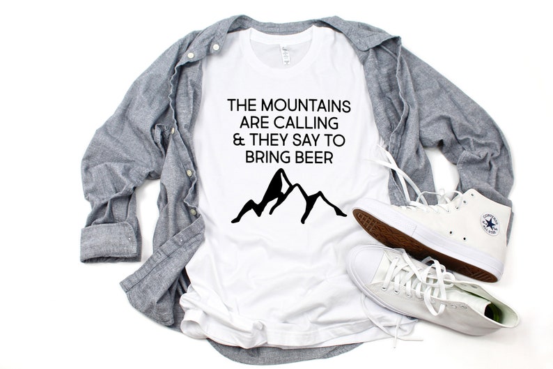 May include: White t-shirt with black text that reads "The mountains are calling & they say to bring beer". A black mountain silhouette is below the text.