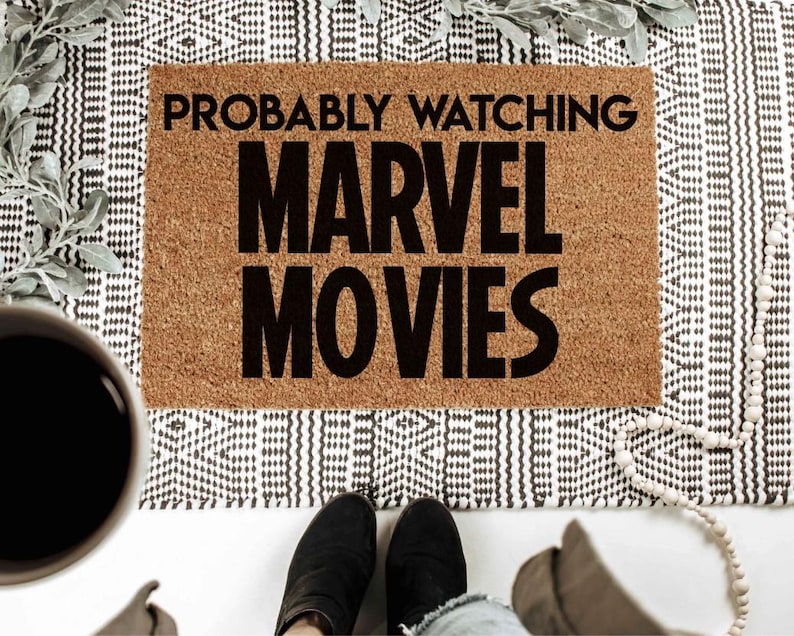 K&ouml;nnte beinhalten: Eine braune Kokosmatte mit dem Text "Probably Watching Marvel Movies" in schwarzen Buchstaben.