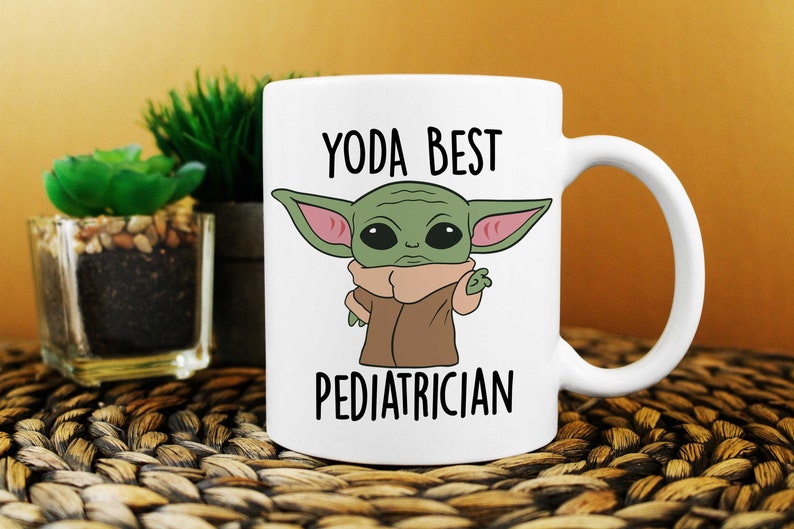 Puede incluir: Taza de cer&aacute;mica blanca con un personaje de dibujos animados verde y el texto "YODA BEST PEDIATRICIAN".