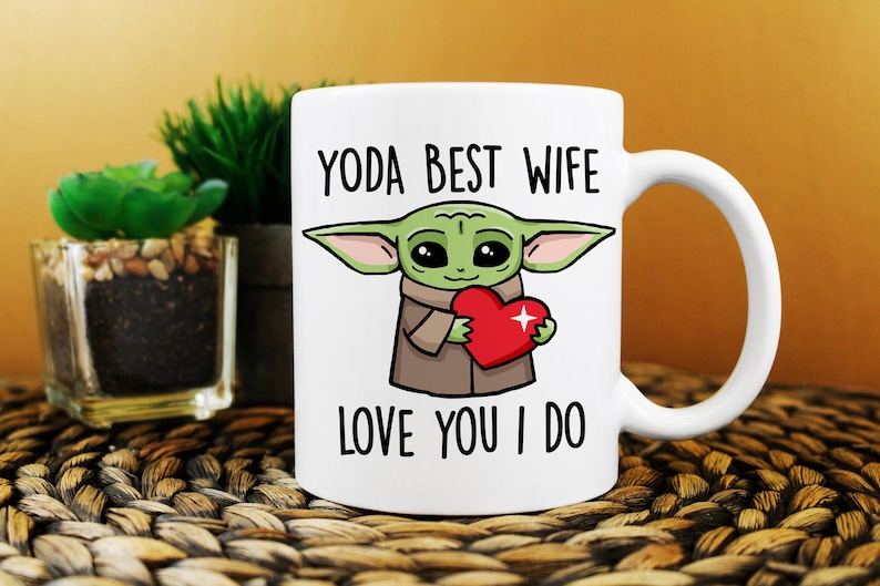 Puede incluir: Taza de cer&aacute;mica blanca con una imagen de dibujos animados de un extraterrestre verde sosteniendo un coraz&oacute;n rojo. El texto "YODA BEST WIFE LOVE YOU I DO" est&aacute; impreso en la taza.