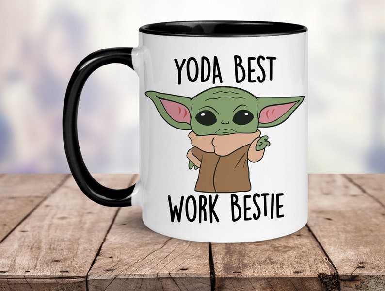 May include: White ceramic mug with a black rim and handle. The mug features a cartoon image of a green alien character with large ears and the text "YODA BEST WORK BESTIE".