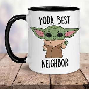 Puede incluir: Taza de cer&aacute;mica blanca con borde y asa negros. La taza presenta una imagen de dibujos animados de un personaje alien&iacute;gena verde con orejas grandes y el texto "YODA BEST NEIGHBOR".