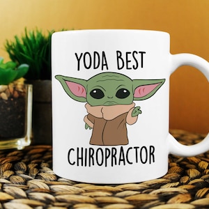 May include: White ceramic mug with a cartoon image of a green alien character with large ears and a brown robe. The text "YODA BEST CHIROPRACTOR" is printed on the mug.