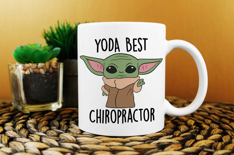 May include: White ceramic mug with a cartoon image of a green alien character with large ears and a brown robe. The text "YODA BEST CHIROPRACTOR" is printed on the mug.
