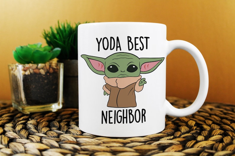 Puede incluir: Taza de cer&aacute;mica blanca con un personaje de dibujos animados verde con orejas grandes y el texto "YODA BEST NEIGHBOR" impreso en ella.