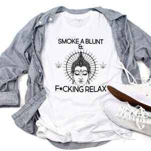 May include: White t-shirt with a black and white illustration of a Buddha with a sunburst behind him. The text "Smoke a blunt & F*cking Relax" is printed on the shirt.