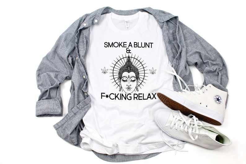 May include: White t-shirt with a black and white illustration of a Buddha with a sunburst behind him. The text "Smoke a blunt & F*cking Relax" is printed on the shirt.