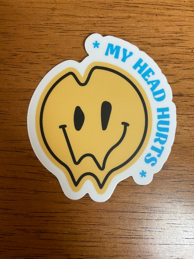 Op de afbeelding: Een gele smiley-sticker met een zwarte omtrek en druppelende randen. De sticker heeft de tekst "* MY HEAD HURTS *" in blauw rond de smiley.