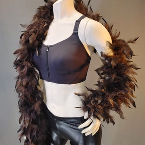 May include: A black sports bra with a zipper closure and brown feather boas. The bra has a high neckline and a racerback style.