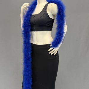 May include: A vibrant blue feather boa draped over a mannequin. The boa is long and fluffy, with a rich, saturated color. The mannequin is wearing a black top and skirt, creating a striking contrast with the boa.