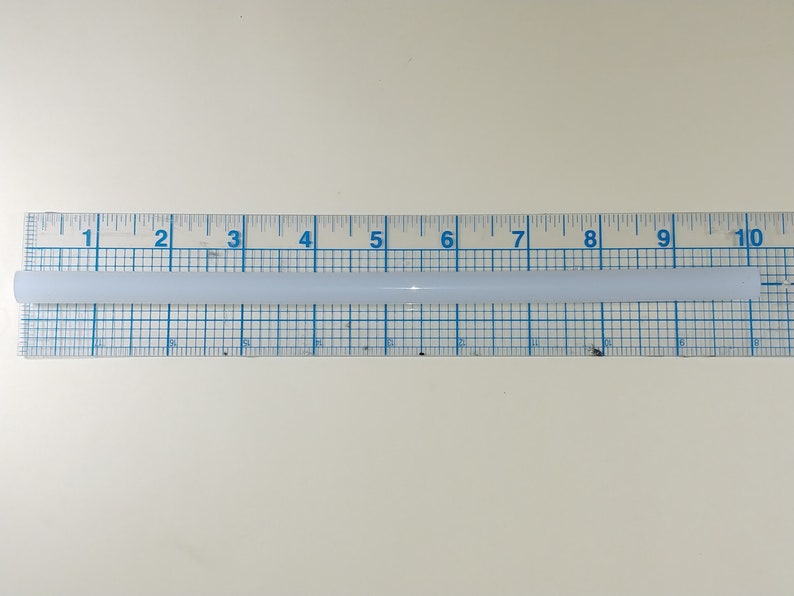 May include: A white glue stick measuring 10 inches in length, placed on a ruler with blue markings.