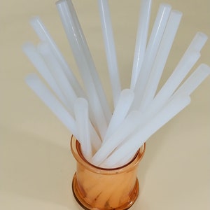 May include: A clear glass jar filled with white glue sticks. The glue sticks are arranged in a radial pattern, with the tips of the sticks pointing outwards.
