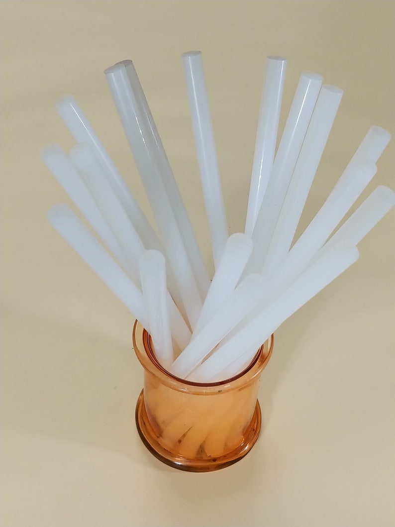 May include: A clear glass jar filled with white glue sticks. The glue sticks are arranged in a radial pattern, with the tips of the sticks pointing outwards.
