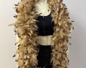 May include: A long, voluminous feather boa featuring a mix of tan, beige, and dark brown speckled feathers. The boa is draped around the neck and shoulders of a mannequin wearing a black zip-up athletic crop top and matching black athletic leggings.