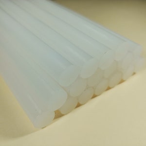 May include: A close-up of a bundle of white glue sticks. The sticks are arranged in a neat stack, with the ends of the sticks visible.
