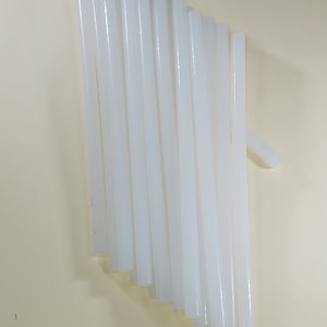 May include: A group of 17 white glue sticks, arranged in a fan shape on a light beige surface.