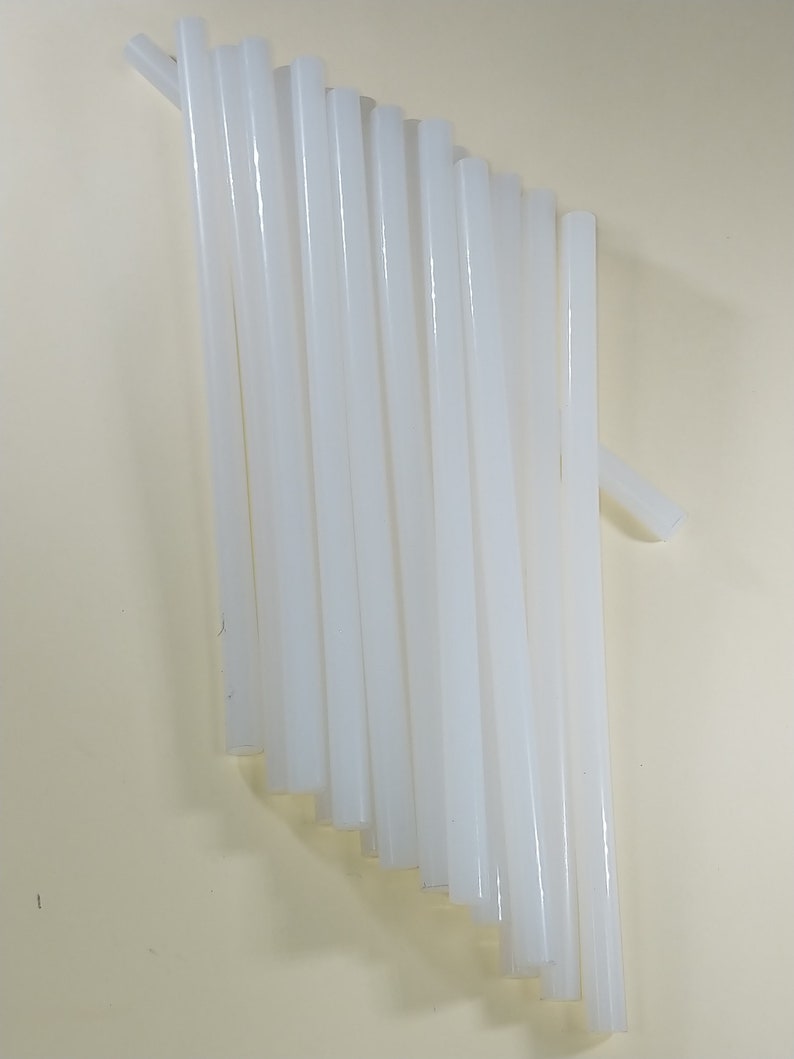 May include: A group of 17 white glue sticks, arranged in a fan shape on a light beige surface.