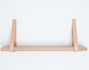 May include: A light wood shelf with two leather straps attached to the wall. The shelf is empty.