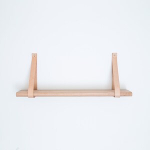 May include: A light wood shelf with two leather straps attached to the wall. The shelf is empty.