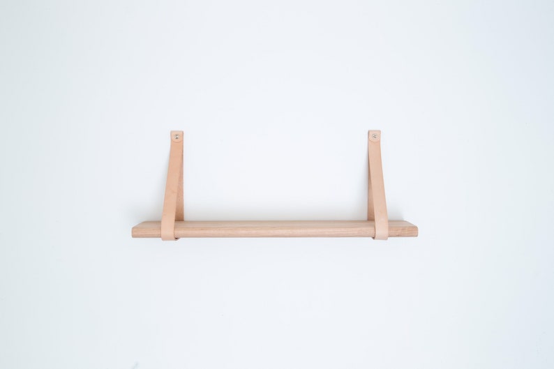 May include: A light wood shelf with two leather straps attached to the wall. The shelf is empty.