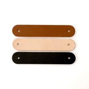 May include: Three leather straps in brown, beige, and black. Each strap has two holes for attaching to a project.