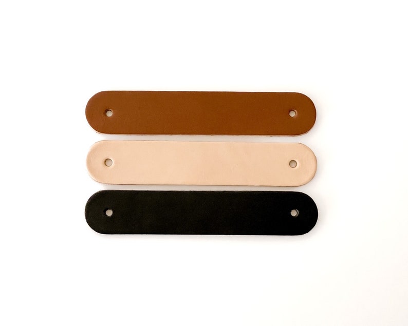 May include: Three leather straps in brown, beige, and black. Each strap has two holes for attaching to a project.