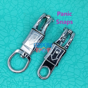 May include: Two silver metal panic snaps, also known as trigger snaps, on a turquoise background. The snaps are designed to quickly and easily connect and disconnect.