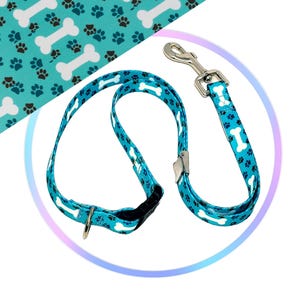 May include: A blue dog leash and collar set with a white bone and paw print pattern. The leash has a silver clip and the collar has a silver D-ring.