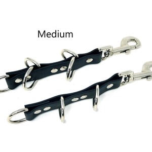 May include: Black leather leash with two metal swivel clips and four metal rings. The leash is labeled "Medium".