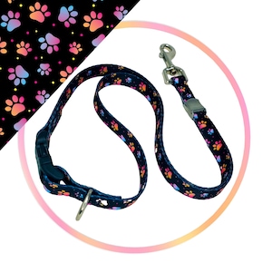 May include: A black dog collar and leash set with a paw print pattern in pink, blue, and orange. The collar has a plastic buckle and the leash has a metal clip.