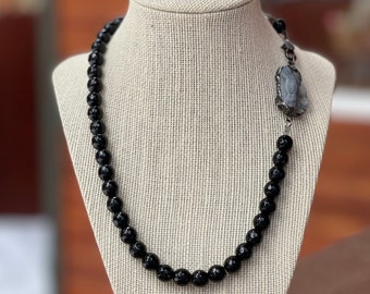 May include: A black onyx beaded necklace with a faceted gray stone pendant. The necklace is displayed on a fabric-covered mannequin.