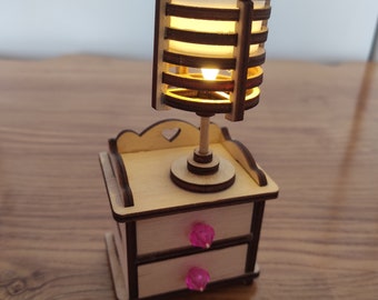 May include: A wooden nightstand with two drawers and a lamp with a slatted shade. The nightstand has pink drawer pulls and the lamp has a warm white light.
