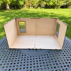 May include: A light-colored wooden dollhouse room structure featuring a flat base and three walls. The two side walls each contain a rectangular window with a grid pattern. The panels are connected with visible interlocking joints at the corners.