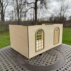 Puede incluir: Un modelo de madera de un edificio con dos ventanas arqueadas. El modelo est&aacute; hecho de madera de color claro y tiene un dise&ntilde;o simple.