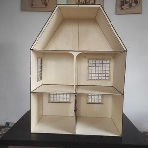 May include: A light-colored wooden dollhouse featuring a two-story structure with an attic space. The interior is divided into four rooms across two levels, each with grid-patterned windows on the walls. The exterior edges are dark-toned.