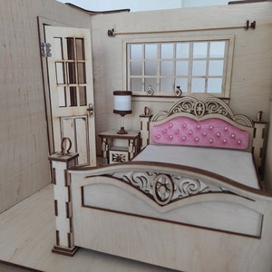 May include: A miniature wooden dollhouse bedroom featuring a bed, bedside table, lamp, and a door. The bed has a pink headboard and a white mattress. The bedside table is made of wood and has a lamp on top.