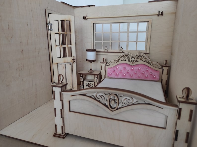 May include: A miniature wooden dollhouse bedroom featuring a bed, bedside table, lamp, and a door. The bed has a pink headboard and a white mattress. The bedside table is made of wood and has a lamp on top.