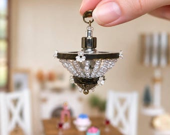 Op de afbeelding: Een miniatuur kroonluchter hanger met een donker metalen frame met een cirkelvormige boven- en onderkant. De structuur is versierd met strengen van kleine, heldere, doorschijnende kralen die tussen de lagen hangen voor een klassiek ontwerp.