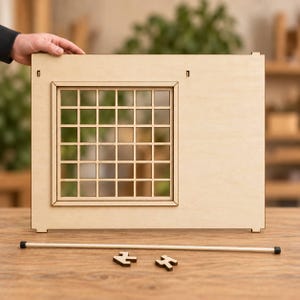May include: A light-colored wooden wall panel featuring a square window with a grid pattern. The panel has two small rectangular slots at the top and two notches at the bottom. A thin wooden rod with black end caps and two small wooden pieces lie below.